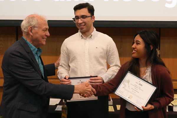 Two M1 students accepting an award for the James D. Popp Summer Research Fellowship while shaking hands with the award presenter